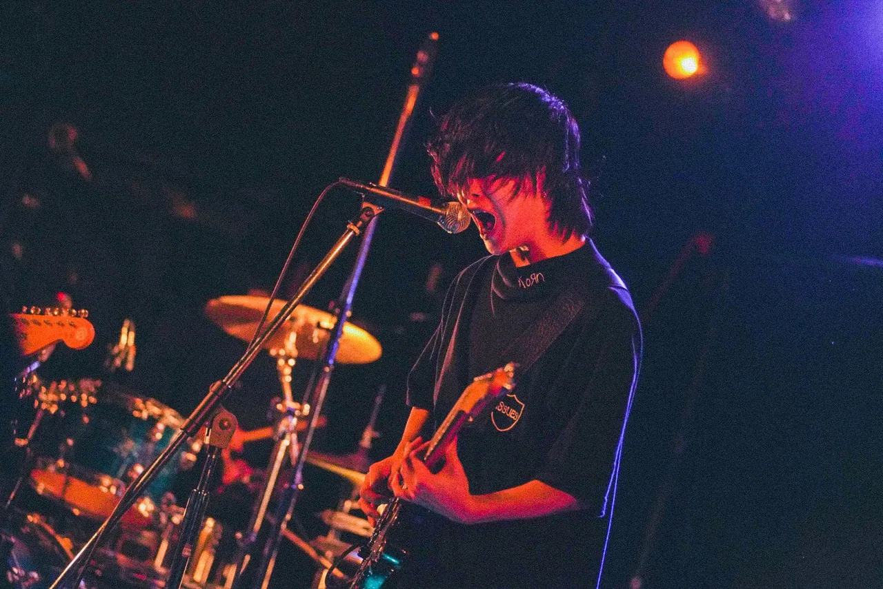 髪で目が隠れたままマイクに叫ぶギタリスト