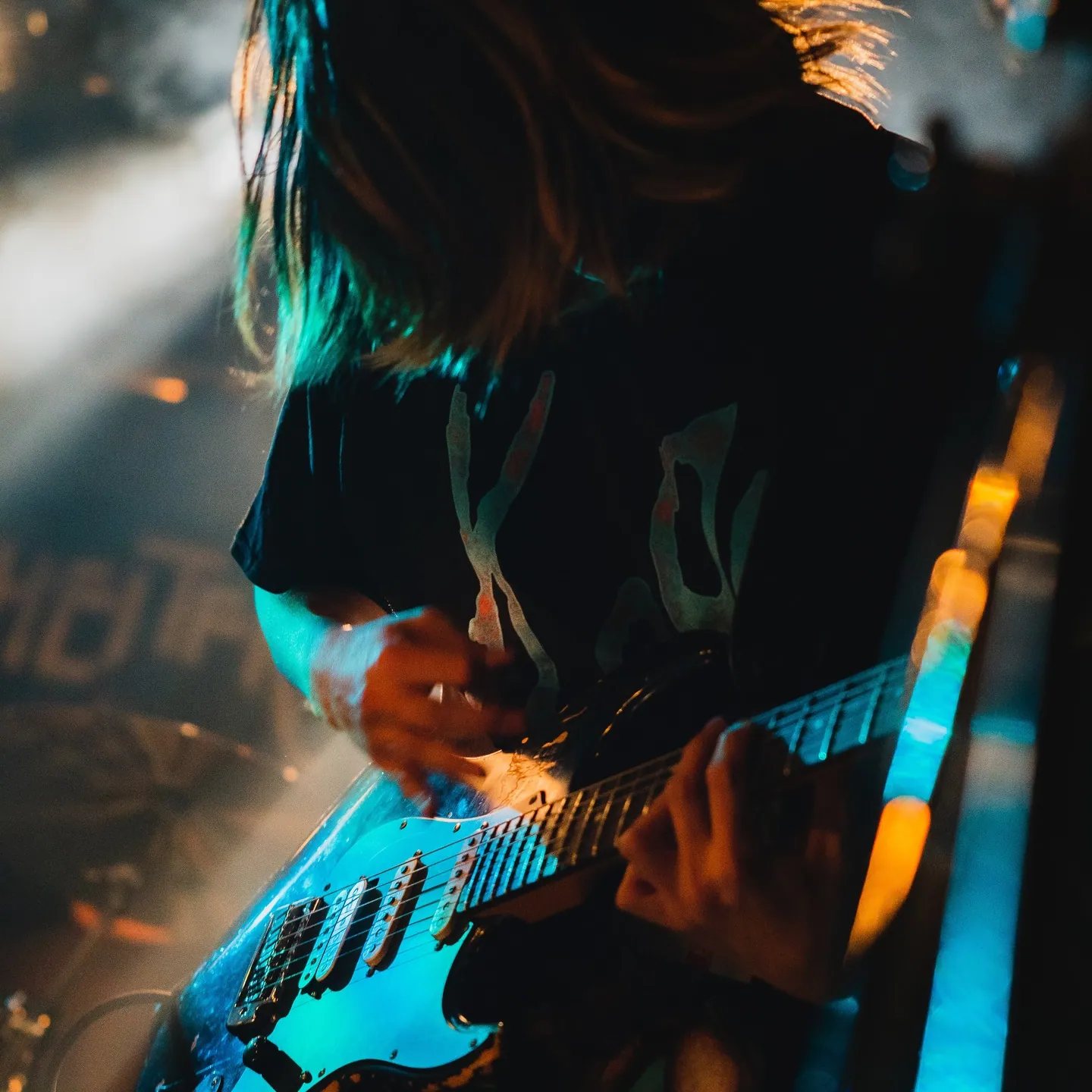 ギターを弾くギタリストの後ろ姿、髪が逆光に透けている